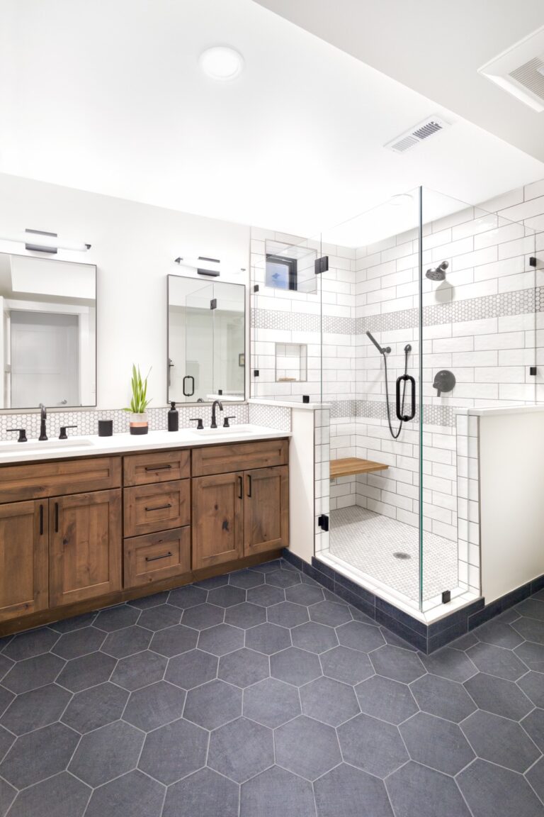 A modern white bathroom with double vanity, white tile backsplash, a standing shower with bench, and rich wood accents.
